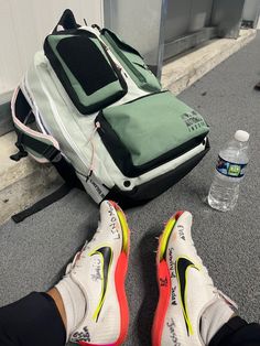 a person's shoes and backpack sitting on the ground next to a water bottle