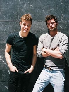 two young men standing next to each other in front of a black and gray wall