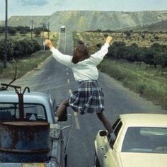 a person jumping in the air over an old truck and other cars on a road