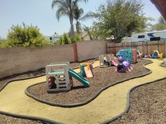 an outdoor play area with toys in the dirt and trees behind it, along with a fence