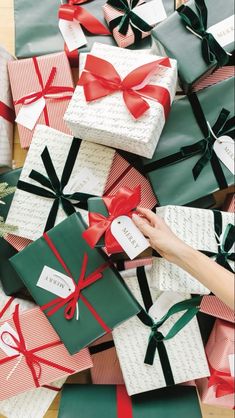 many wrapped presents with red and green bows on them are being held by someone's hand