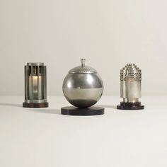 three silver objects sitting on top of a white table next to candles and vases