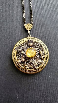 Large Flower Locket Necklace This necklace locket is bronze and copper, decorated with beautiful thistle flower that gives a vintage style cottage vibe. The piece is very involved and carefully made with a lot of detail. A lovely locket Necklace showcasing a yellow stone. See Photos for size comparison against American quarter Chain: ~ Antique Bronze Choose YOUR CHAIN LENGTH during checkout ☻More Lockets Here: https://www.etsy.com/shop/FashionCrashJewelry/search?search_query=lockets&order=date_d Luxury Vintage Round Pendant Locket Necklace, Steampunk Gold Jewelry With Antique Finish, Bronze Steampunk Jewelry With Engraving, Steampunk Bronze Engraved Jewelry, Antique Gold Steampunk Jewelry As Gift, Antique Gold Steampunk Jewelry Gift, Antique Gold Steampunk Jewelry For Gift, Antique Copper Locket Jewelry, Steampunk Antique Gold Jewelry Gift