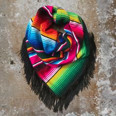 a multicolored scarf with fringes hanging on a concrete wall in the daytime