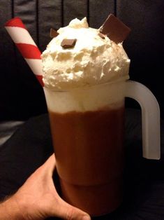 a hand holding a cup with whipped cream and chocolate