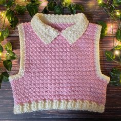 a pink and white sweater sitting on top of a wooden table next to green leaves