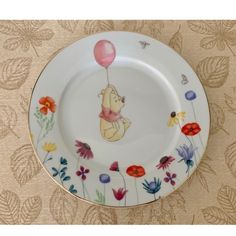 a plate with winnie the pooh holding a pink balloon on it's side