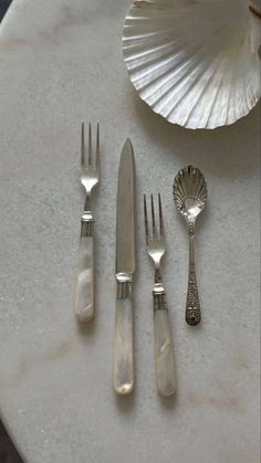 four forks, two spoons and one knife sitting on a table next to a seashell