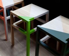 three different colored stools sitting next to each other on a wooden floor in front of a black wall