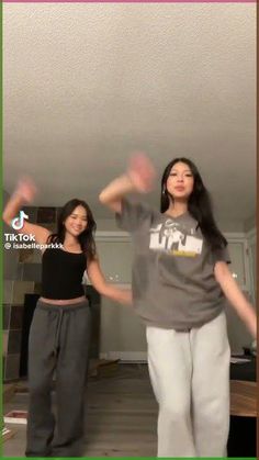 two young women are dancing in the living room with their hands up and one is holding her arms out