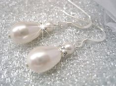 two white pearls are hanging from silver earwires on a piece of glass cloth