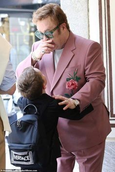 a man in a pink suit is talking to a little boy wearing a black backpack