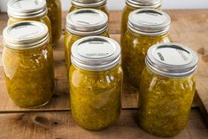 six jars filled with pickles sitting on top of a wooden table next to each other