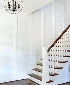 a white staircase with wooden handrails and chandelier