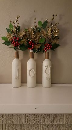 three bottles with flowers in them sitting on a mantle