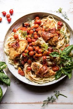 a plate of pasta with meat, tomatoes and herbs on it next to some greens