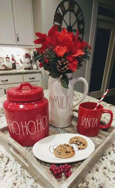 a tray with cookies and mugs sitting on top of a kitchen counter next to a vase filled with poinsettis