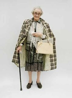 an old woman holding a cane and looking at her cell phone while standing in front of a white wall