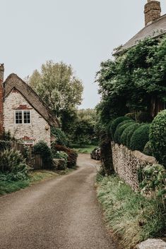 a stone house with a thatched roof next to a gravel road in the countryside