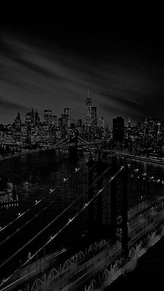 black and white photograph of the brooklyn bridge at night with city lights in the background