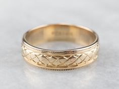 a gold wedding ring with intricate designs on the inside and outside, sitting on a white surface