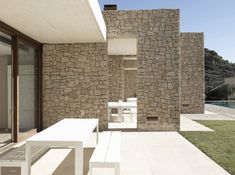 an outdoor dining area with white tables and chairs, next to a wall made out of rocks