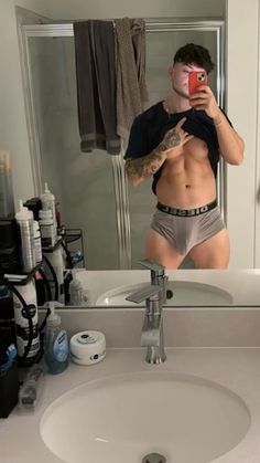 a man taking a selfie in front of a bathroom mirror with his shirt off