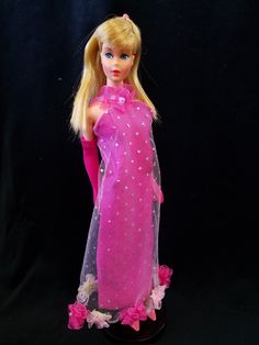 a barbie doll wearing a pink dress with flowers on the bottom and long blonde hair