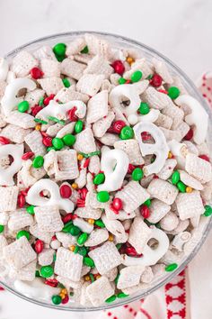 a glass bowl filled with white and green candy cornflakes, m & m's and pretzels