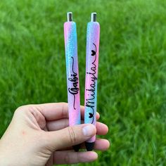 two pink and blue pens with writing on them are held in front of the camera