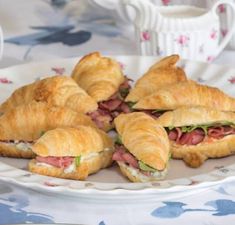 sandwiches on croissants with meat and cheese are arranged on a plate next to a cup