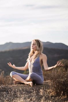 a woman sitting in the middle of a field doing yoga