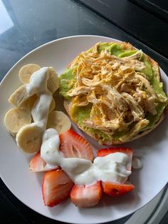 a white plate topped with a sandwich covered in cream next to sliced strawberries and bananas