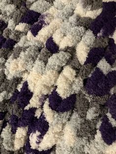 a close up view of a crocheted blanket with purple and white flowers on it