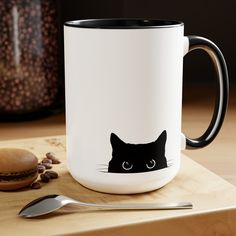 a coffee mug with a black cat's face on it next to a spoon