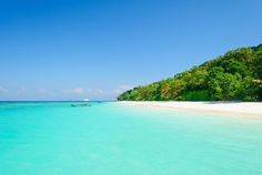 the water is crystal blue and there are people in the boat out on the beach