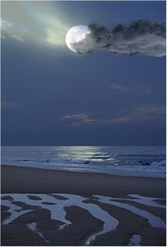 the moon is setting over the ocean with clouds in the sky and water on the beach