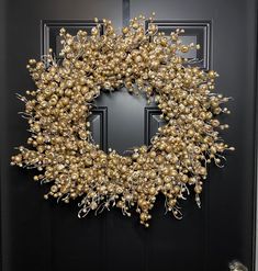 a wreath is hanging on a door with gold balls and silver ribbon around it,