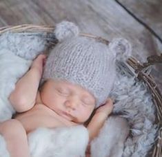 a baby is sleeping in a basket wearing a knitted bear hat and white fur