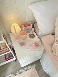 a white table topped with lots of items next to a pink lamp and pillow on top of a bed