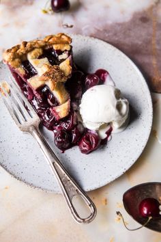 a piece of pie on a plate with ice cream and cherries next to it