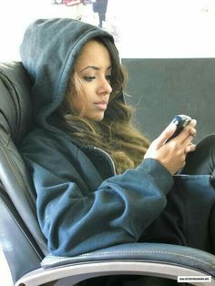 a woman sitting in a chair looking at her cell phone while wearing a hoodie