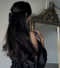 a woman with long black hair standing in front of a mirror looking at her reflection