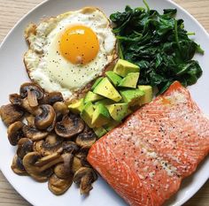 a white plate topped with salmon, mushrooms and an egg next to spinach leaves