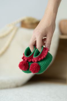 a hand holding a pair of crocheted slippers with pom - poms