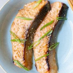 two pieces of fish on a blue plate with chopsticks next to the dish