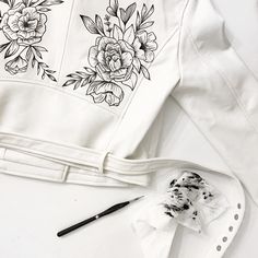 a white jacket with flowers painted on it next to a paintbrush and some other items