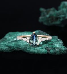 an engagement ring with a pear shaped blue and white diamond in the center on top of a green rock