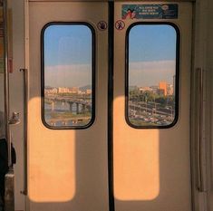 two double doors on a train with the view of a bridge in the distance and cars passing by