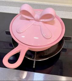 a pink cooking pot with a bow on the lid sitting on top of a stove